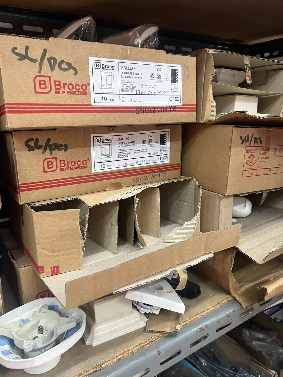 Dus saklar Broco Galleo double switch dan fitting lampu tersusun di rak toko